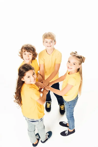 Visão de alto ângulo de adoráveis crianças felizes empilhando as mãos e sorrindo para a câmera isolada no branco — Fotografia de Stock