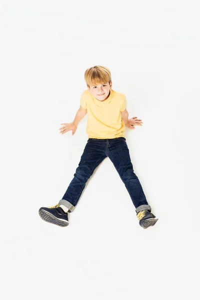 Vista de ángulo alto de adorable niño feliz sentado y sonriendo a la cámara aislado en blanco - foto de stock