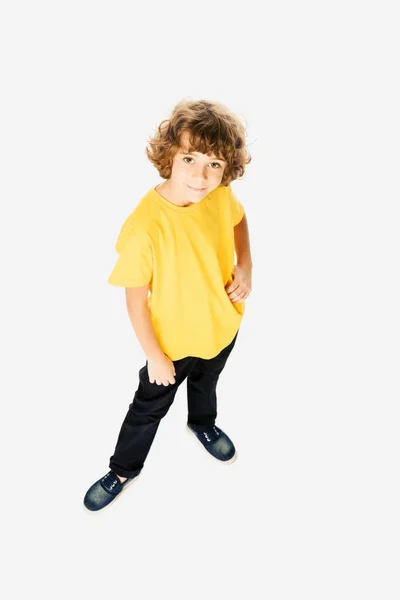 Vista de ángulo alto de lindo niño de pie con la mano en la cintura y sonriendo a la cámara aislada en blanco - foto de stock