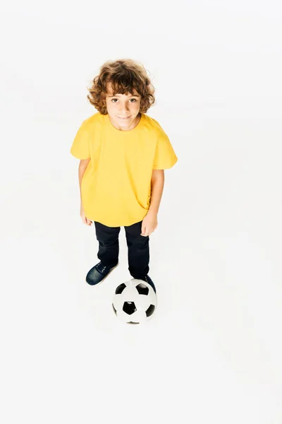 Hochwinkelaufnahme des niedlichen kleinen Jungen, der mit Fußball steht und isoliert auf Weiß in die Kamera lächelt — Stockfoto