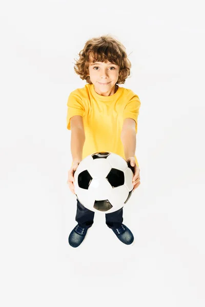 Vista de ángulo alto de adorable niño sosteniendo pelota de fútbol y sonriendo a la cámara aislada en blanco - foto de stock