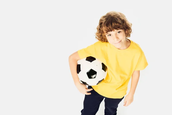 Vista de ángulo alto de niño pequeño sosteniendo pelota de fútbol y sonriendo a la cámara aislada en blanco — Stock Photo