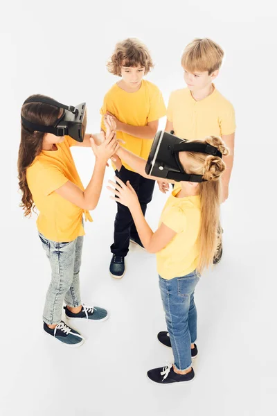 Vista de ángulo alto de niños adorables usando auriculares de realidad virtual aislados en blanco - foto de stock