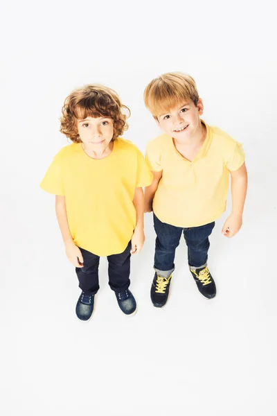 Vista de ángulo alto de dos niños felices de pie juntos y sonriendo a la cámara aislada en blanco - foto de stock