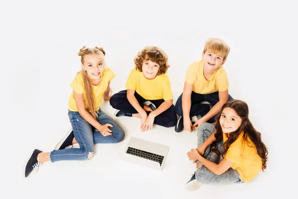 Vista de ángulo alto de los niños felices usando el ordenador portátil y sonriendo a la cámara aislada en blanco - foto de stock