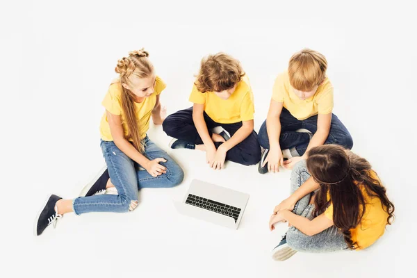 Високий кут зору групи милих дітей, що сидять і використовують ноутбук разом ізольовані на білому — стокове фото