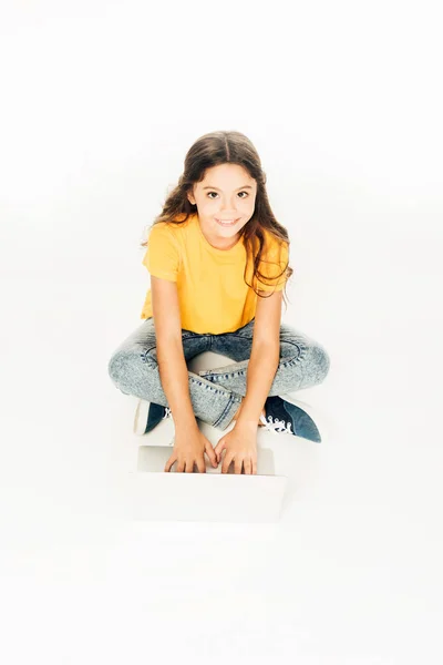 High angle view of adorable happy kid using laptop and smiling at camera isolated on white — Stock Photo