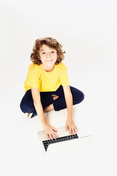 Visão de alto ângulo do menino feliz usando laptop e sorrindo para a câmera isolada no branco — Fotografia de Stock