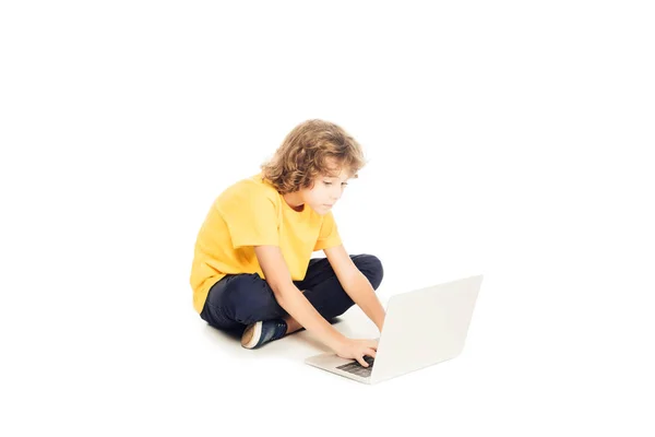 Adorable little boy sitting and using laptop isolated on white — Stock Photo