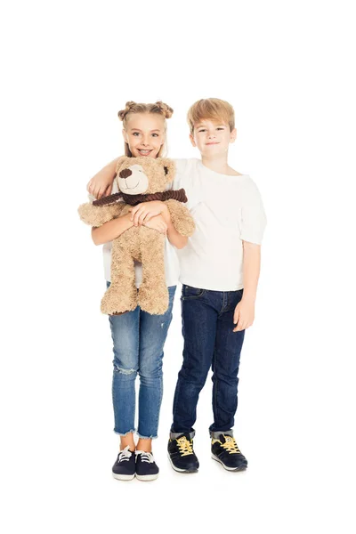 Lächelnde Kinder, die sich umarmen, einen Teddybär in der Hand halten und isoliert auf weiß in die Kamera schauen — Stockfoto