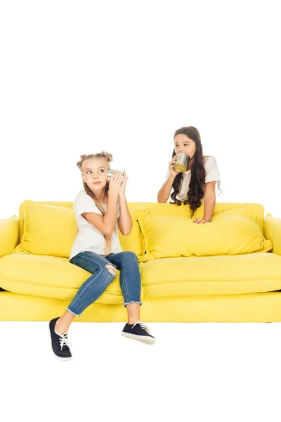 Kids playing with tin cans phone on yellow sofa isolated on white — Stock Photo