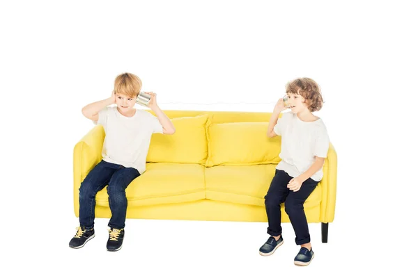 Adorable boys playing with tin cans phone on yellow sofa isolated on white — Stock Photo