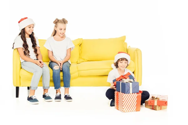 Souriant enfants regardant garçon dans santa chapeau avec des cadeaux isolés sur blanc — Photo de stock