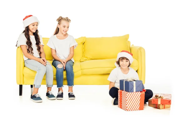 Niños sonrientes mirando a niño en sombrero de santa con regalos aislados en blanco - foto de stock