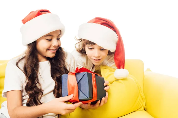 Excited adorable kids in santa hats looking at present isolated on white — Stock Photo