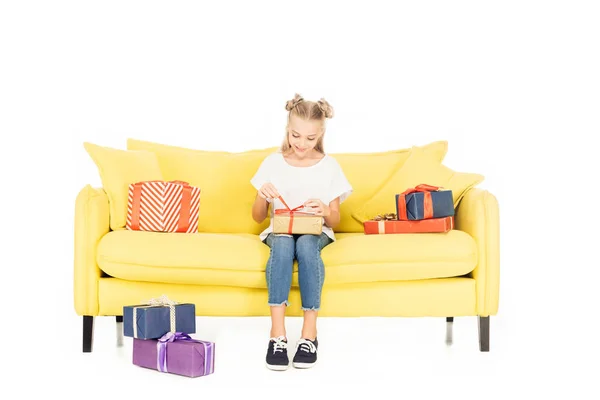 Criança adorável sorrindo abertura presente no sofá amarelo isolado no branco — Fotografia de Stock