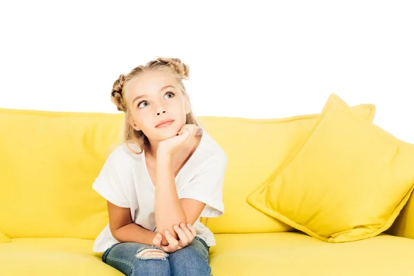 Bambino adorabile pensoso seduto sul divano giallo e guardando in alto isolato sul bianco — Foto stock