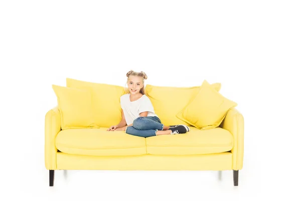 Entzückendes Kind sitzt auf gelbem Sofa und blickt isoliert auf weiße Kamera — Stockfoto