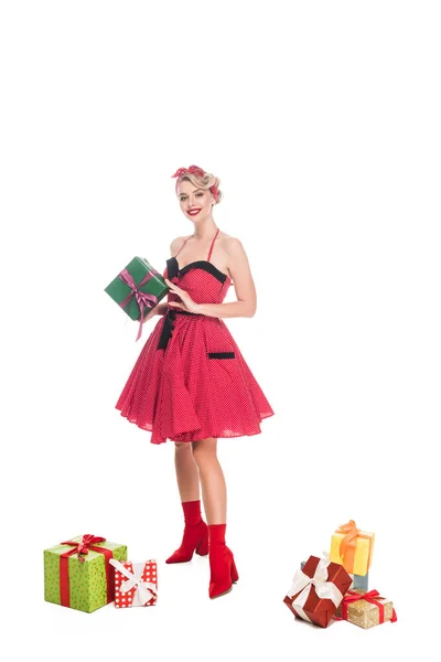 Smiling young pin up woman standing near pile of gift boxes isolated on white — Stock Photo