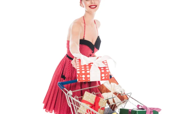 Partial view of pin up woman carrying shopping cart with pile of gift boxes and giving present isolated on white — Stock Photo