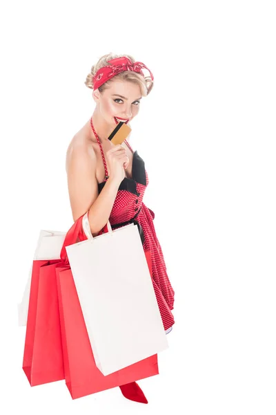 Vista de ángulo alto de la mujer en la ropa pin up con bolsas de compras morder tarjeta de crédito aislado en blanco - foto de stock