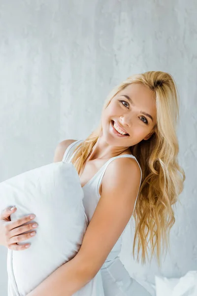 Beautiful happy blonde girl in underwear holding pillow and smiling at camera — Stock Photo