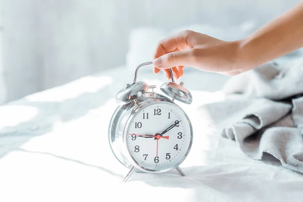 Vista parcial de cerca de la joven mujer sosteniendo el reloj despertador en el dormitorio — Stock Photo