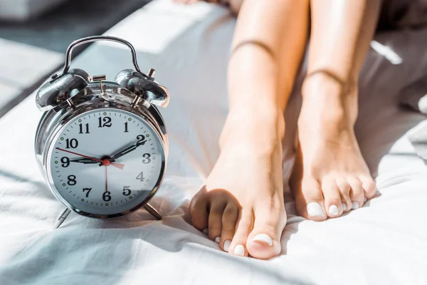 Крупным планом частичный вид женских ног и будильник на кровати — стоковое фото