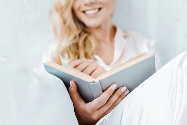 Close-up view of happy young woman in pajamas sitting and reading book — Stock Photo