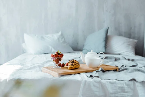 Croissant, strawberries and tea on wooden tray on bed — Stock Photo