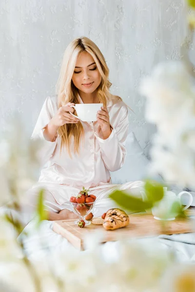 Schöne Frau im Pyjama trinkt morgens Tee im Bett — Stockfoto