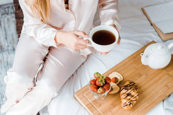 Обрізане зображення жінки в піжамі, що тримає чашку чаю в ліжку вранці — стокове фото