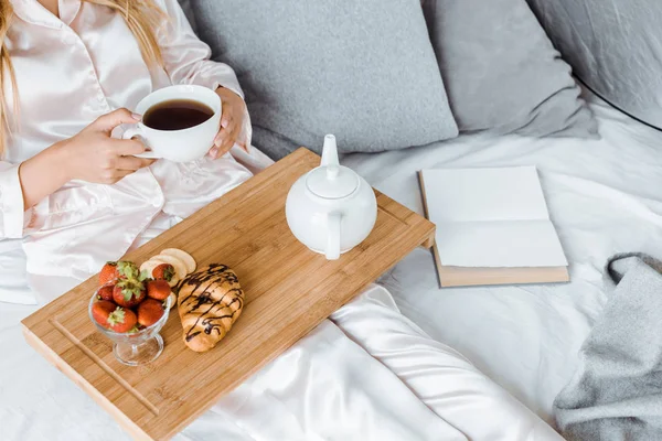 Geschnittenes Bild einer Frau im Pyjama, die im Bett frühstückt und eine Tasse Tee hält — Stockfoto