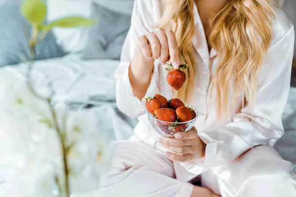 Imagem cortada de mulher em pijama segurando morangos na cama de manhã — Fotografia de Stock