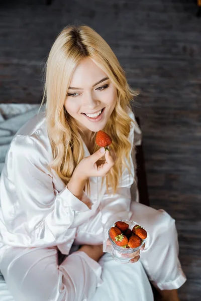 Vista ad alto angolo di donna attraente in pigiama mangiare fragola a letto al mattino — Foto stock