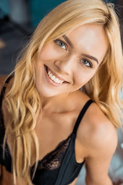 Portrait of attractive smiling woman in black lingerie looking at camera in bedroom — Stock Photo