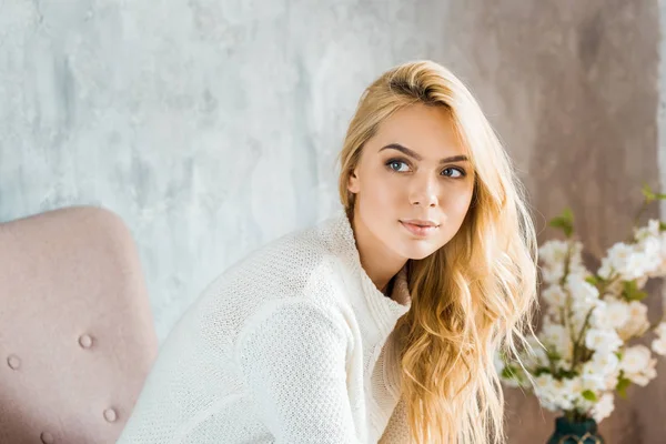 Portrait of beautiful woman in sweater sitting on armchair in bedroom and looking away — Stock Photo