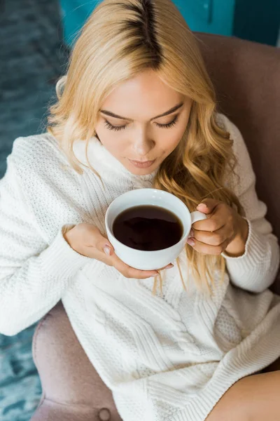 Vista de ángulo alto de la mujer atractiva en suéter beber té en el dormitorio por la mañana - foto de stock