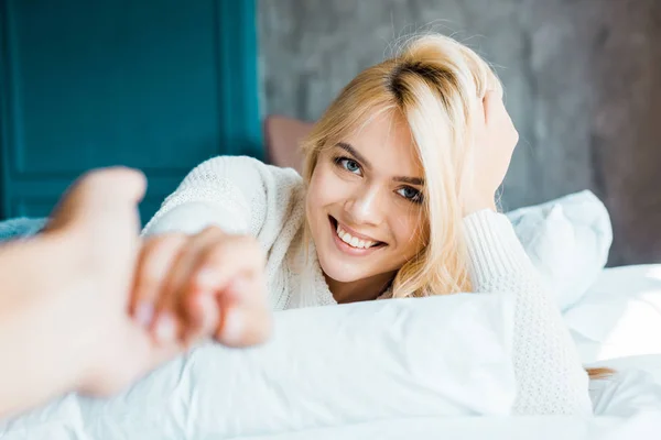 Imagen recortada de novio y novia atractiva en suéter tomados de la mano en el dormitorio - foto de stock
