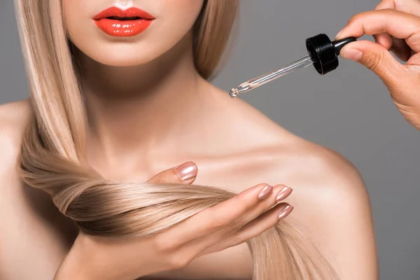 Abgeschnittene Aufnahme von Kosmetikerin Anwendung von Lotion auf Haare von schönen Mädchen isoliert auf grau — Stockfoto