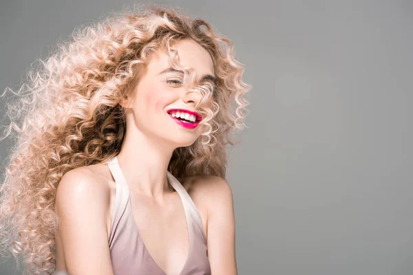 Porträt einer glücklichen jungen Frau mit langen lockigen Haaren, die isoliert auf grau lacht — Stockfoto