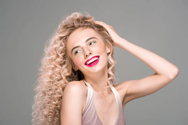 Hermosa chica feliz con el pelo largo rizado riendo y mirando hacia otro lado aislado en gris - foto de stock