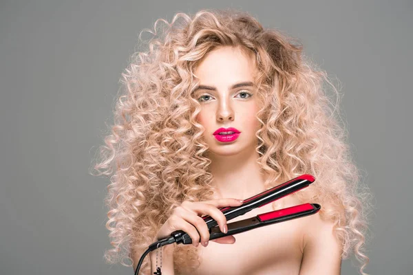 Linda menina nua com cabelos longos encaracolados segurando alisador de cabelo e olhando para a câmera isolada no cinza — Fotografia de Stock