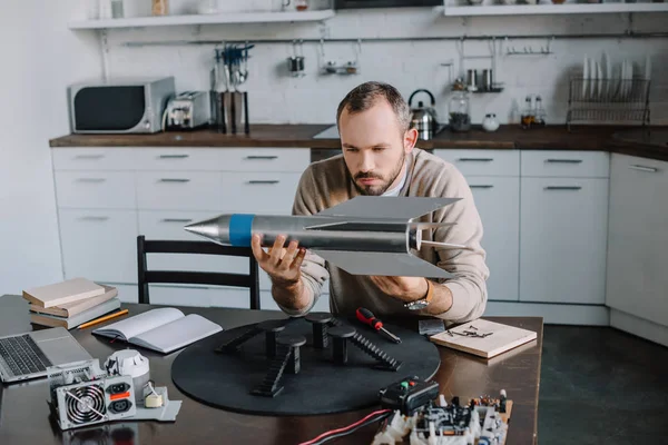 Handsome engineer looking at rocket model at home — Stock Photo