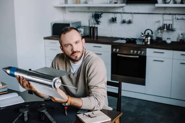 Schöner Ingenieur mit Raketenmodell zu Hause und Blick in die Kamera — Stockfoto