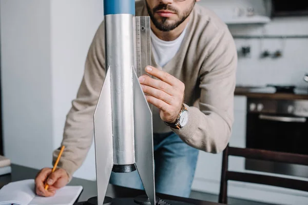 Обрезанное изображение инженера моделирования ракеты и измерения с линейкой в домашних условиях — стоковое фото