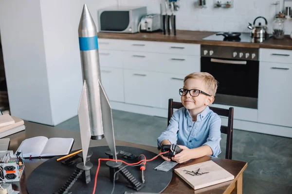 Entzückender Junge sitzt am Tisch und testet Raketenmodell am Wochenende in der Küche — Stockfoto