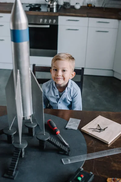 Чарівний хлопчик сидить за столом з ракетною моделлю на кухні у вихідні — стокове фото