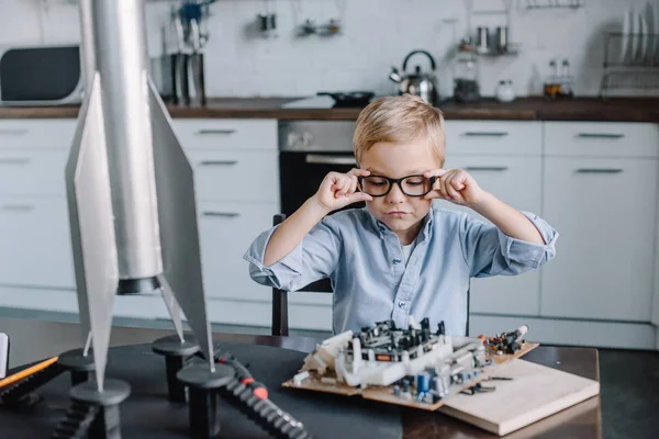 Entzückender Junge, der am Wochenende Brille anfasst und Platine in Küche betrachtet — Stockfoto