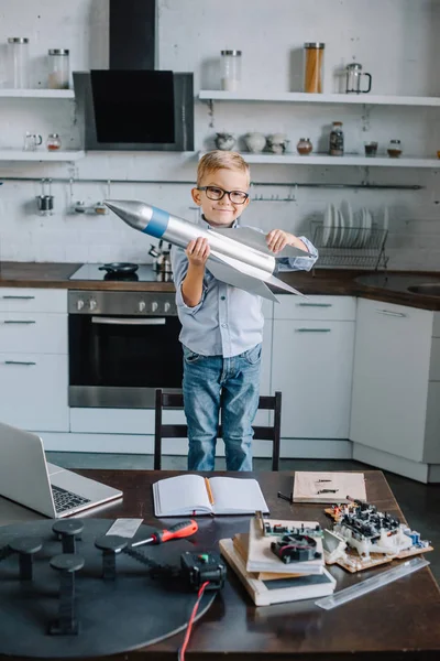 Entzückender Junge hält Raketenmodell in der Küche und schaut in die Kamera — Stockfoto